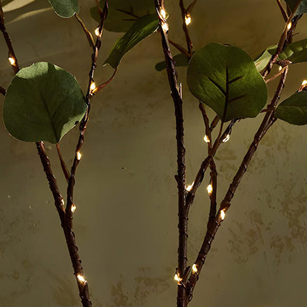 Sfeervolle LED bloemenlichtjes rond een vaas met groene takken, perfect voor een gezellige en warme ambiance.