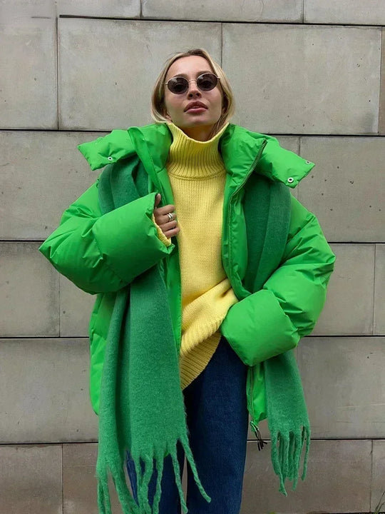 Vrouw draagt een stijlvolle gewatteerde winterjas, ideaal voor koude dagen. De jas is oversized en comfortabel, met een royale capuchon voor extra warmte en bescherming tegen de kou. Ze combineert de jas met een gebreide muts, zonnebril en casual outfit, wat een modieuze en warme uitstraling creëert. Perfect voor winterse wandelingen en dagelijkse activiteiten in de kou.